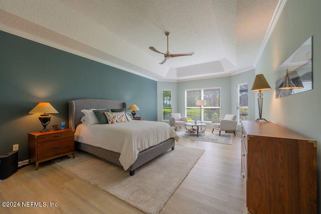 bedroom featuring ceiling fan, a tray ceiling, a textured ceiling, and light hardwood / wood-style flooring