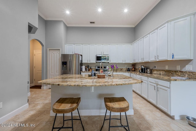 kitchen with appliances with stainless steel finishes, white cabinetry, a kitchen island with sink, and light stone counters