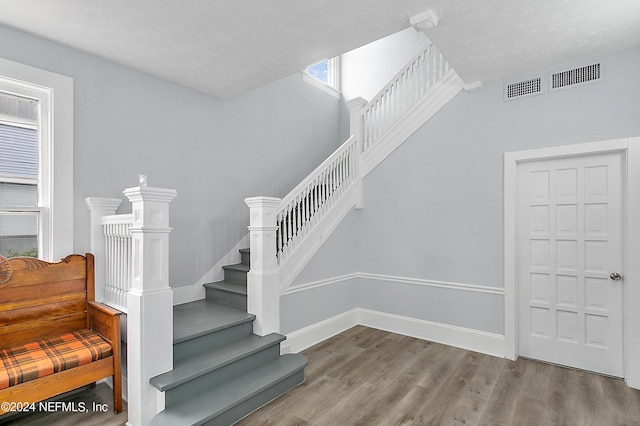 stairway featuring baseboards, a textured ceiling, visible vents, and wood finished floors