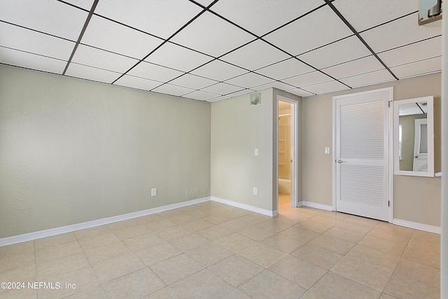 unfurnished room featuring a paneled ceiling, light tile patterned floors, and baseboards