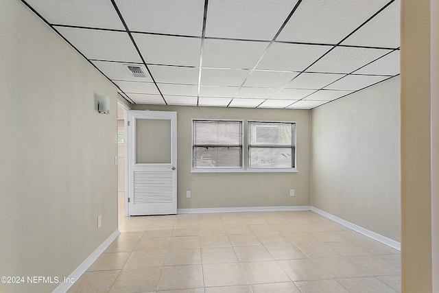 empty room with a paneled ceiling, baseboards, visible vents, and light tile patterned flooring