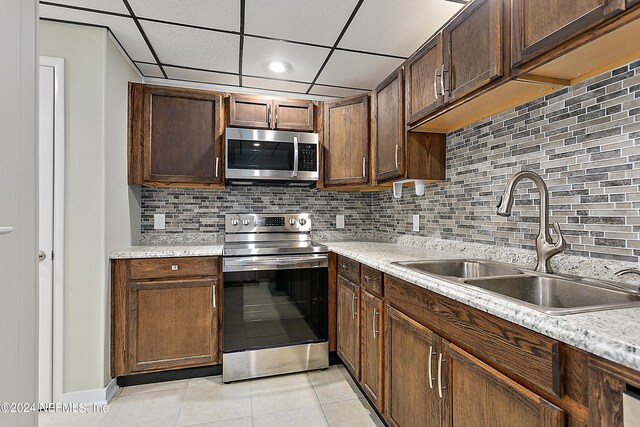 kitchen featuring stainless steel appliances, light tile patterned floors, decorative backsplash, a paneled ceiling, and sink