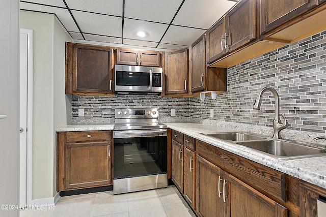 kitchen with stainless steel appliances, tasteful backsplash, light countertops, light tile patterned flooring, and a sink