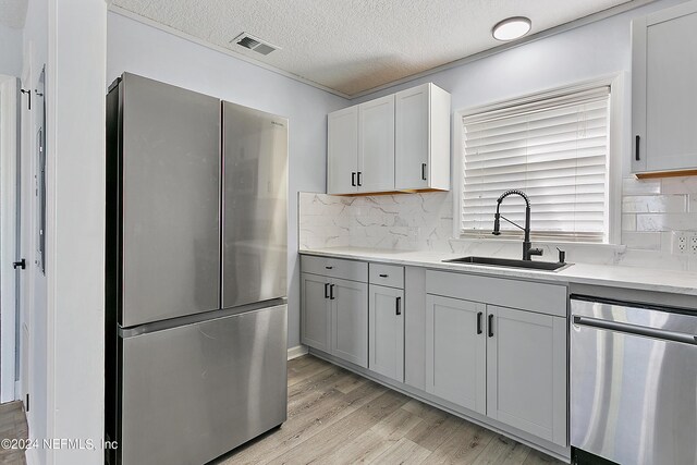 kitchen with light hardwood / wood-style flooring, a textured ceiling, appliances with stainless steel finishes, backsplash, and sink