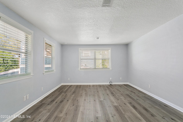 empty room featuring a wealth of natural light, baseboards, visible vents, and hardwood / wood-style floors