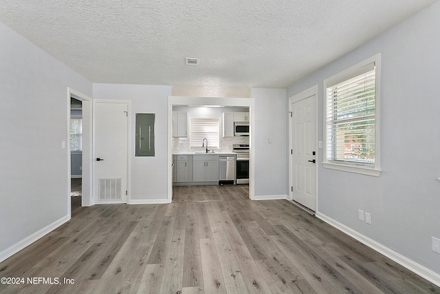 unfurnished living room with light wood-type flooring, electric panel, visible vents, and a sink