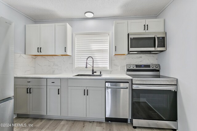 kitchen featuring crown molding, stainless steel appliances, a textured ceiling, sink, and light hardwood / wood-style flooring