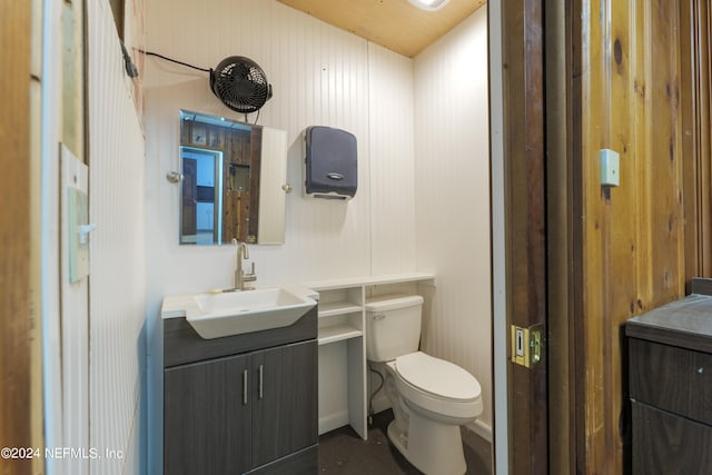 bathroom with vanity, wooden walls, and toilet