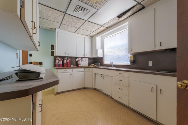 kitchen with backsplash, a paneled ceiling, sink, and white cabinetry