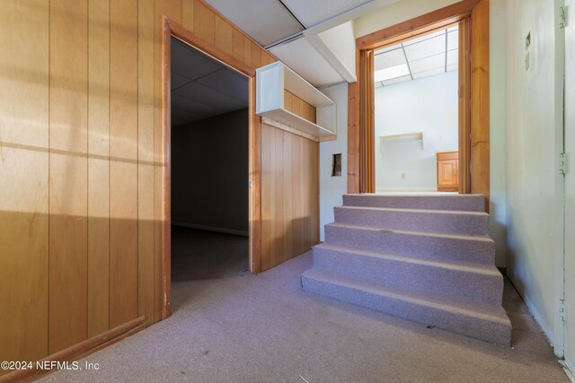 staircase with wooden walls, carpet, and a paneled ceiling