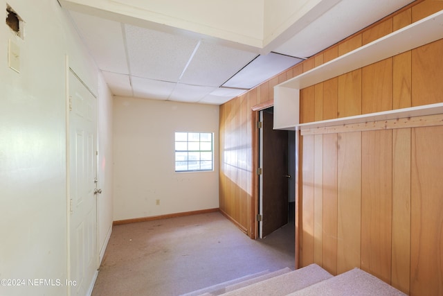 unfurnished bedroom with a paneled ceiling, wood walls, light carpet, and baseboards