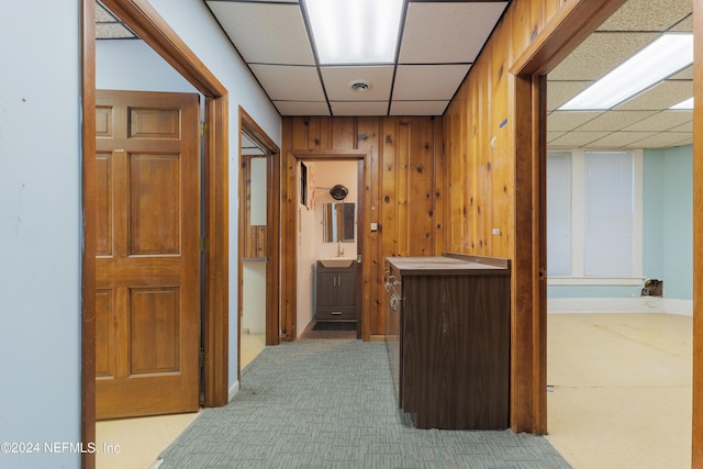 corridor with a paneled ceiling, wood walls, carpet floors, and a sink