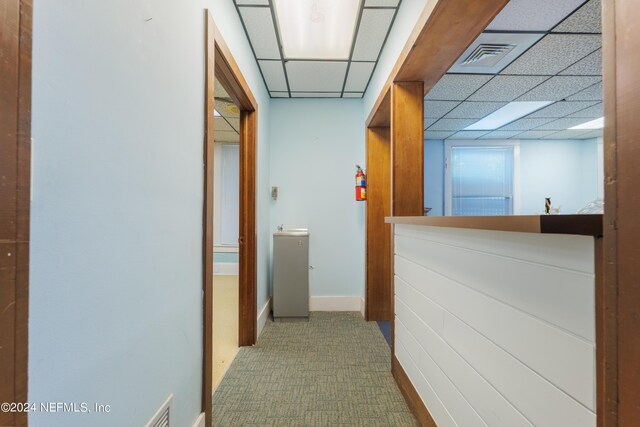 hall with carpet and a paneled ceiling