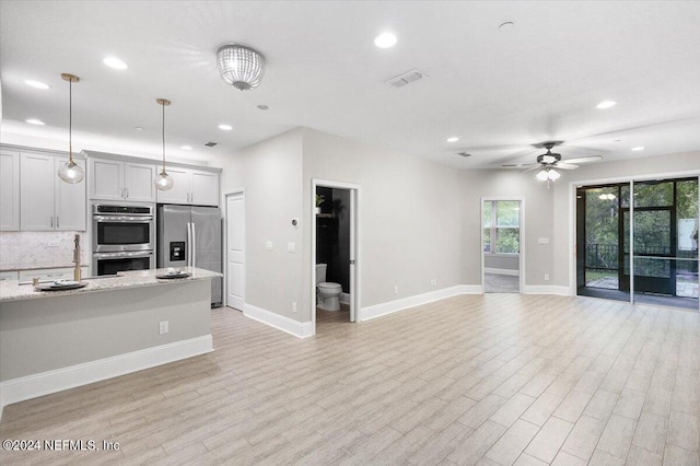 kitchen with light wood-style floors, open floor plan, appliances with stainless steel finishes, decorative backsplash, and pendant lighting