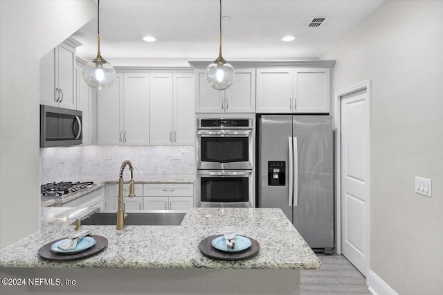 kitchen featuring light stone counters, stainless steel appliances, a sink, visible vents, and decorative light fixtures