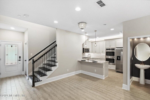 kitchen with light wood finished floors, visible vents, backsplash, appliances with stainless steel finishes, and a peninsula