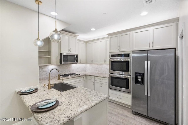 kitchen featuring a peninsula, a sink, light stone countertops, stainless steel appliances, and backsplash