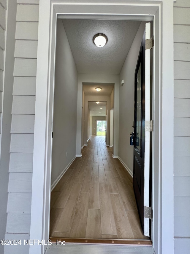 hall with a textured ceiling and light hardwood / wood-style flooring