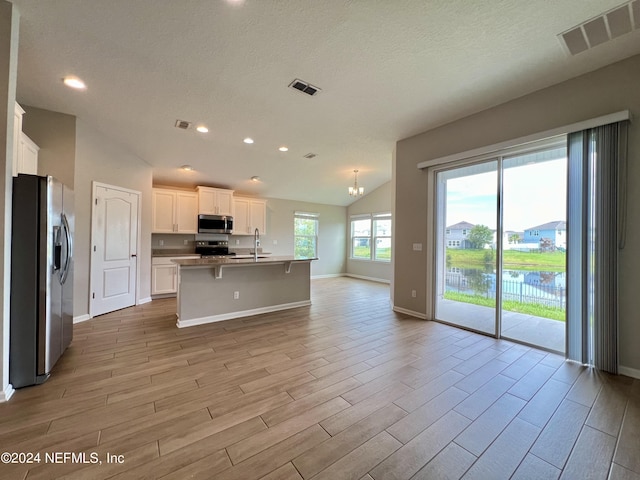 kitchen with a breakfast bar area, appliances with stainless steel finishes, light hardwood / wood-style floors, an island with sink, and white cabinets