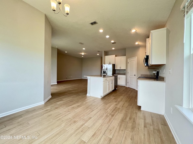 kitchen with light hardwood / wood-style flooring, appliances with stainless steel finishes, a kitchen island with sink, a textured ceiling, and white cabinets