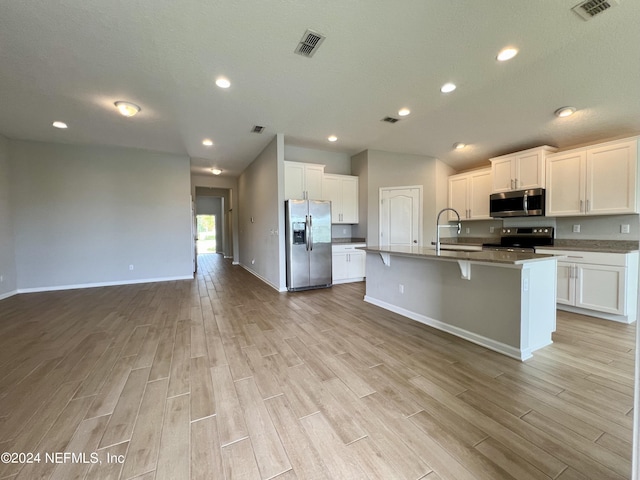 kitchen with white cabinetry, appliances with stainless steel finishes, a kitchen island with sink, and light wood-type flooring