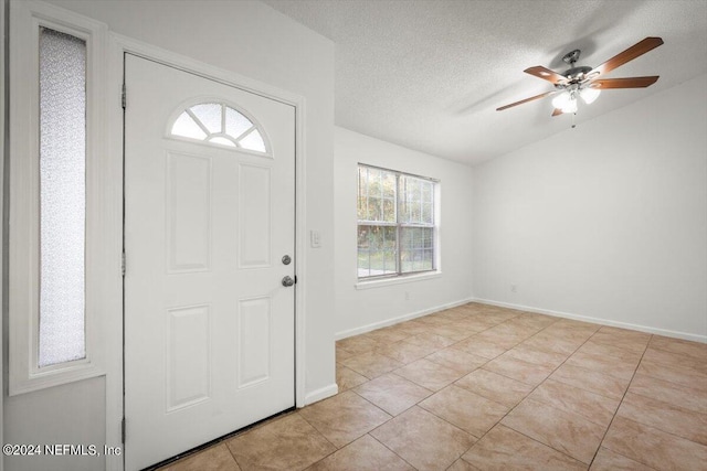 foyer entrance with a textured ceiling, light tile patterned floors, a wealth of natural light, and ceiling fan