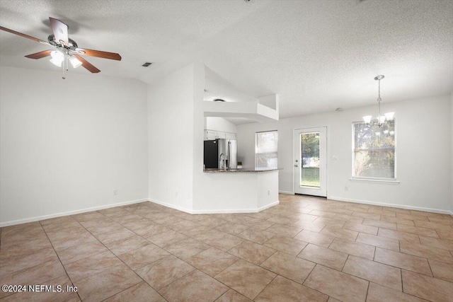 unfurnished living room with a textured ceiling, ceiling fan with notable chandelier, vaulted ceiling, and light tile patterned floors