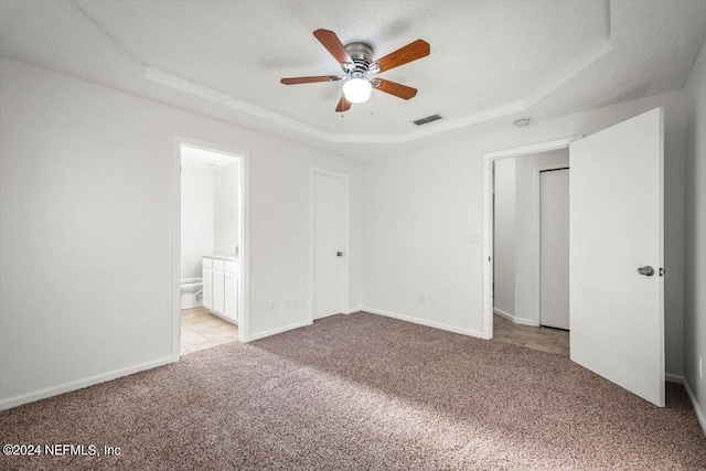 unfurnished bedroom featuring ceiling fan, ensuite bathroom, and a tray ceiling