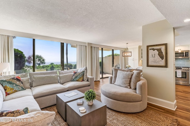 living room featuring an inviting chandelier, a textured ceiling, baseboards, and wood finished floors