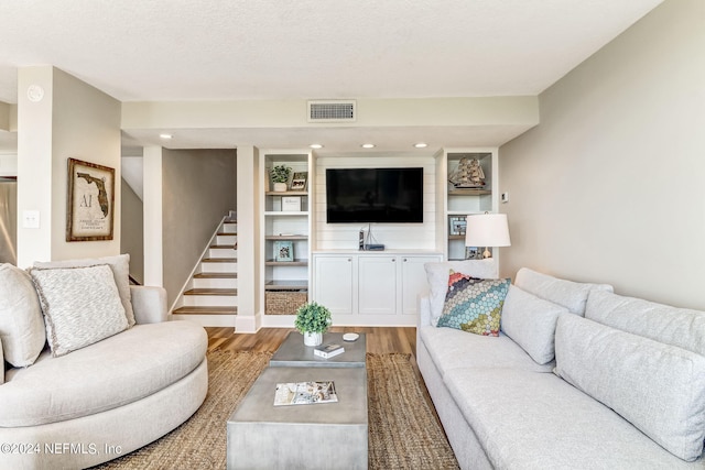 living room featuring visible vents, stairway, a textured ceiling, light wood-type flooring, and baseboards