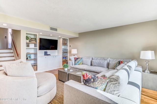 living room with visible vents, a textured ceiling, light wood finished floors, and stairs