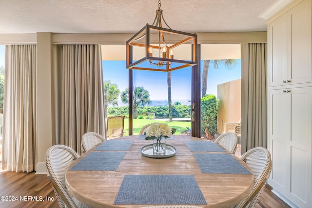 dining space with dark wood-style floors, a textured ceiling, and a notable chandelier