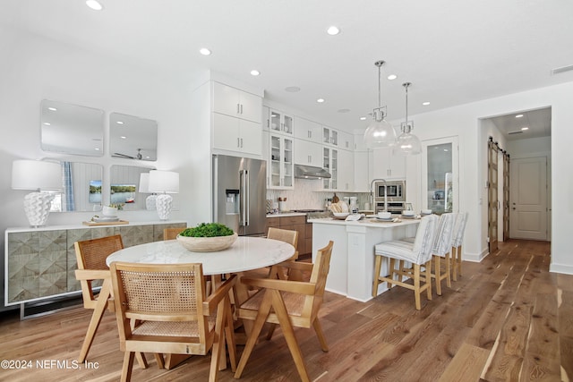 dining area with recessed lighting, baseboards, light wood-type flooring, and a barn door