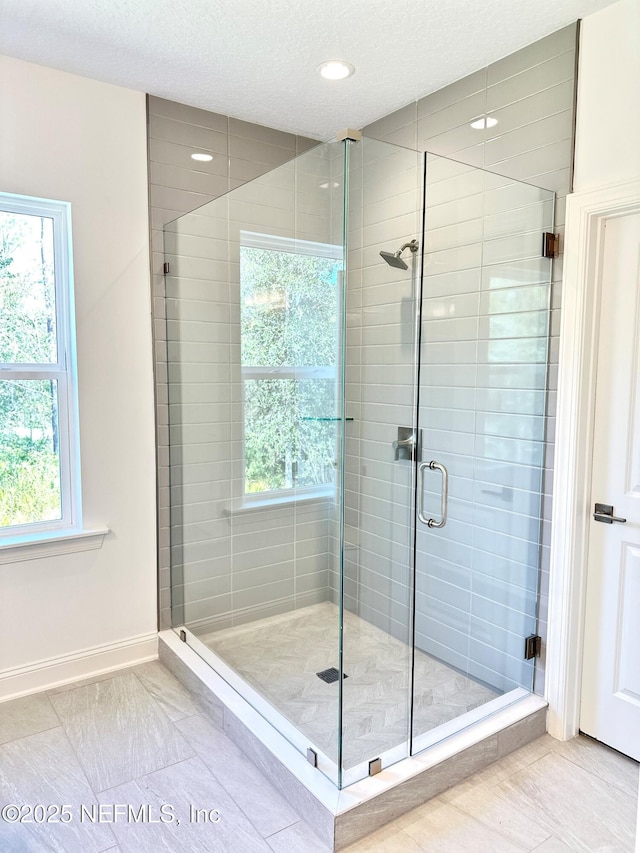 full bath featuring baseboards, a textured ceiling, a stall shower, and tile patterned flooring