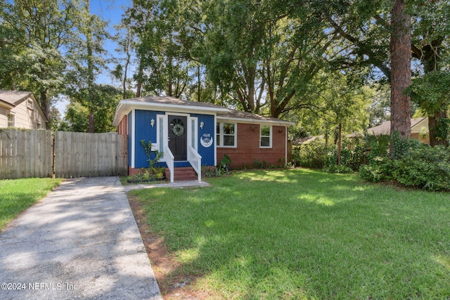 view of front of property featuring brick siding, fence, aphalt driveway, and a front yard