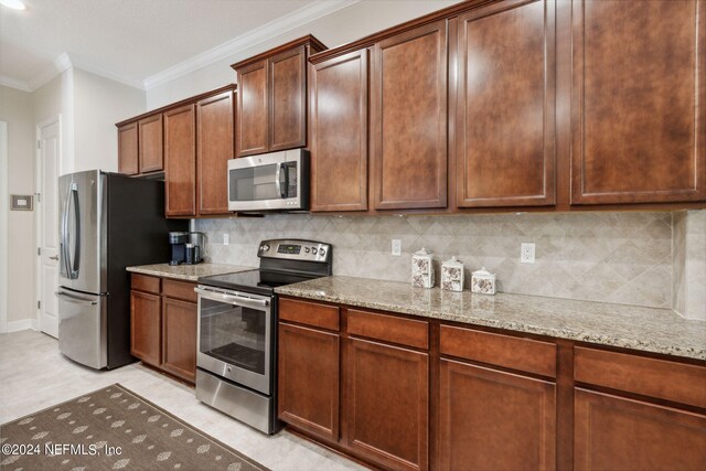 kitchen featuring stainless steel appliances, light stone counters, crown molding, decorative backsplash, and light tile patterned flooring