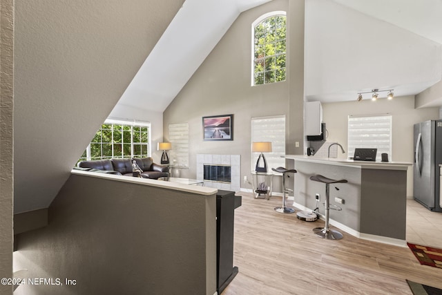 living room featuring high vaulted ceiling, a fireplace, light hardwood / wood-style floors, and sink