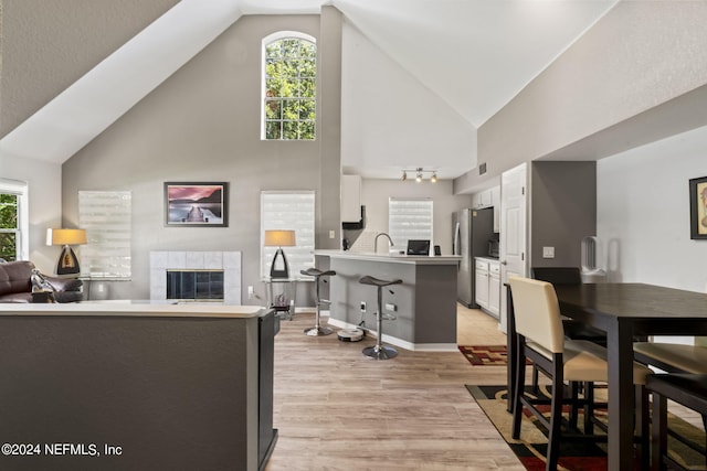 living room featuring sink, high vaulted ceiling, a fireplace, and light hardwood / wood-style floors