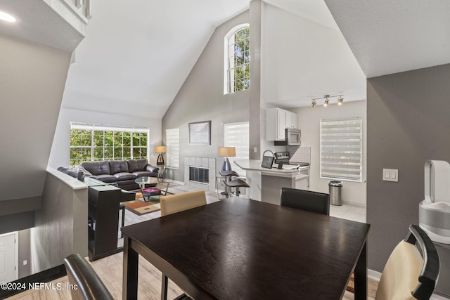 dining space with a tiled fireplace and high vaulted ceiling