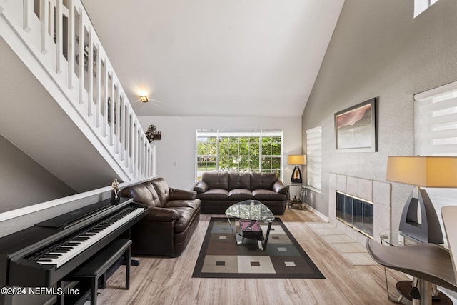 living room with high vaulted ceiling, a tiled fireplace, and light hardwood / wood-style floors