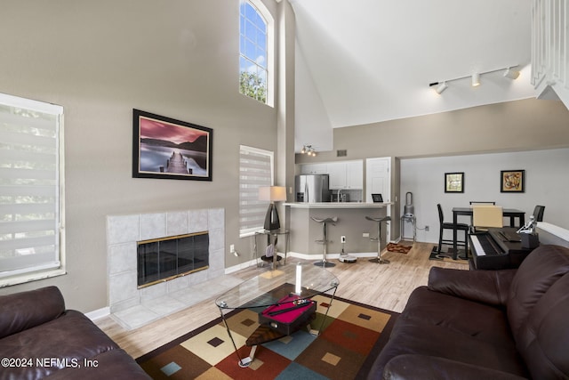 living room with a tiled fireplace, track lighting, a high ceiling, and light wood-type flooring