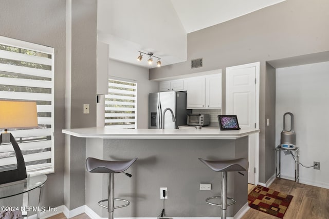 kitchen with tasteful backsplash, white cabinets, a kitchen bar, kitchen peninsula, and stainless steel refrigerator with ice dispenser