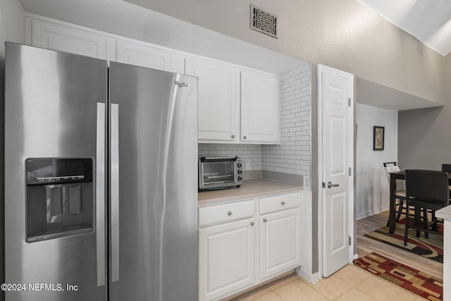 kitchen with backsplash, stainless steel fridge, light tile patterned floors, and white cabinets