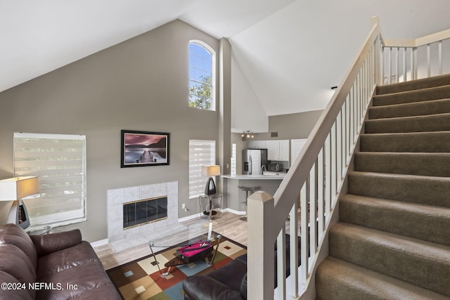 living room featuring a tiled fireplace, hardwood / wood-style floors, and high vaulted ceiling