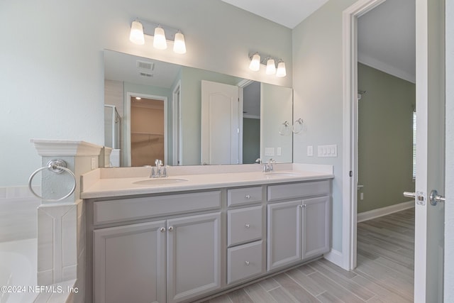 bathroom with a garden tub, double vanity, wood finished floors, and a sink