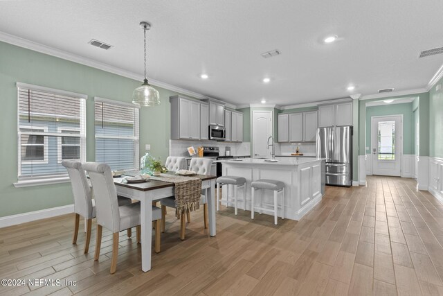 dining area with light wood-style floors, visible vents, and crown molding