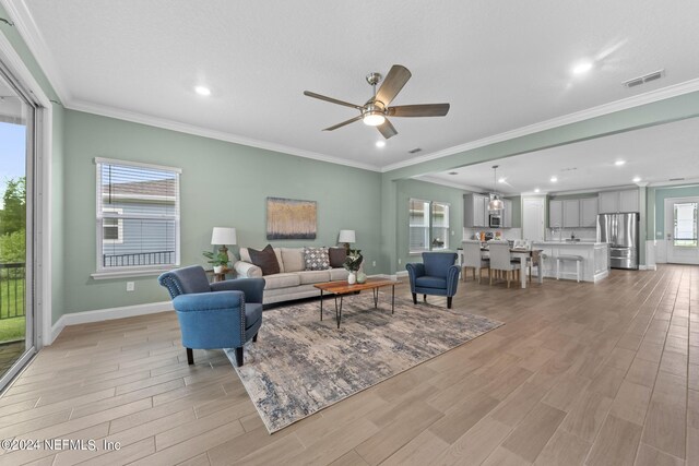 living room featuring visible vents, ornamental molding, light wood-style flooring, and baseboards