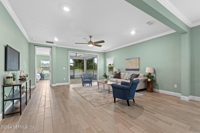 living room featuring visible vents, baseboards, a ceiling fan, light wood-style flooring, and ornamental molding