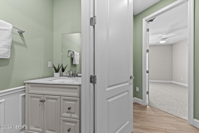 bathroom with a ceiling fan, vanity, baseboards, and wood finished floors