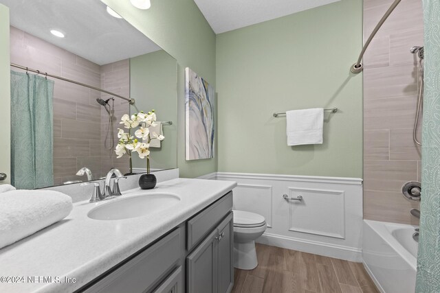 bathroom with wainscoting, toilet, wood finished floors, shower / bathtub combination with curtain, and vanity